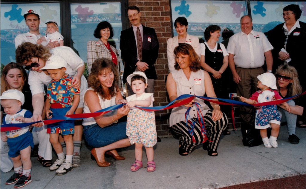 This 1996 photo is from the June 1st opening festivities for the CAW Oshawa Child Care Facilities. The first child enrolled is shown front/centre. Also taking part are child care centre workers and, in the back row (l to r) : unidentified man; Laurel Rothman, director of CAW childcare services; Jim Cameron of General Motors; Peggy Nash, assistant to CAW President; unidentifed woman; Dave Broadbent, CAW Local 222 secretary-treasurer; and Nancy Diamond, Oshawa Mayor. The photo is from the CAW Archives.