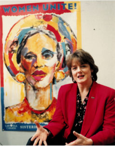 This is an undated photo of Canadian Auto Workers (CAW) activist and feminist, Peggy Nash. Peggy is sitting in front of the powerful CAW Women Unite Sisterhood Solidarity painting.