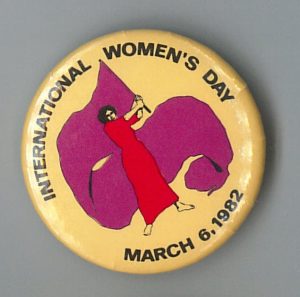 Button was used for the 1982 International Women's Day March in Toronto. The image of the woman waving a large flag links International Women's Day to early socialist celebrations.