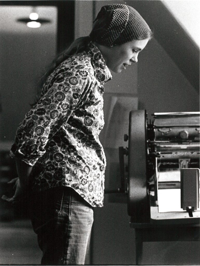 Cathy Carroll, now Billie Carroll, working on office Gestetner at the Women's Press office on Bloor Street West in Toronto. Photo from between 1972-1976. Photograph by Janice Acton.