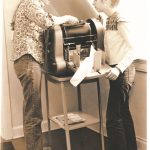 Cathy Carroll, now Billie Carroll, and Kathy Jackman working on the Gestetner at the Women's Press office on Bloor Street in Toronto. Photo taken between 1972 and 1976.