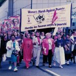 Photo taken at Women's March Against Poverty – For Bread and Roses, For Jobs and Justice.” The cross-country action was organized by the Canadian Labour Congress and the National Action Committee on the Status of Women in 1996. Right to left: Frances Lankin, Judy Darcy, Mary Ismail (holding banner), Nancy Riche, Louisette Hinton, Angie Schera, Sunera Thobani, Sue Carter (holding banner at left), June Veecock. Alexa McDonough, leader of the federal NDP is also visible between Sunera Thobani and Angie Schera.